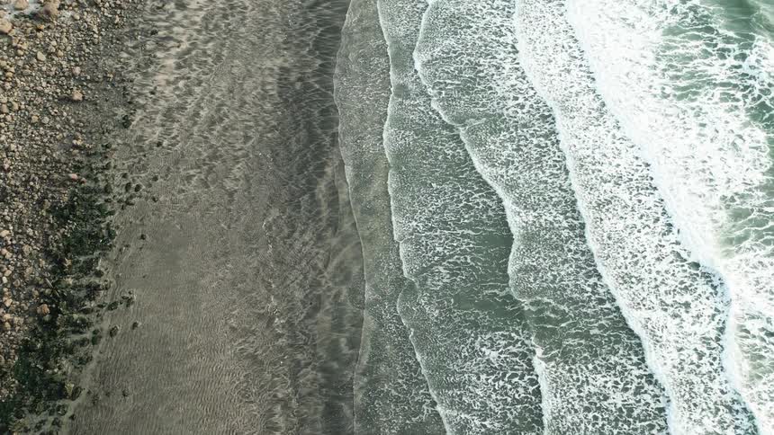 Aerial of a sandy beach and cliffsides while ocean waves roll into the shore
