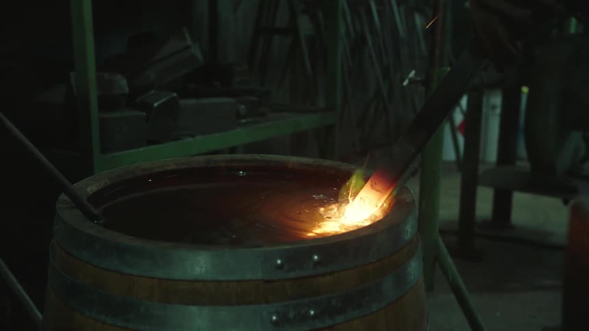 Closeup of a mans arm grabbing a hot iron and placing it into a barrel of water