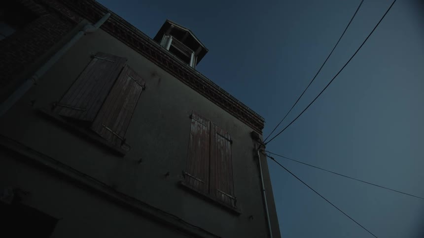 Wooden shutters are closed on two windows of an apartment building on a clear day