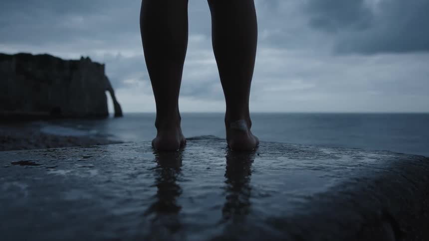 Closeup of a womans legs on top of a rock by the sea