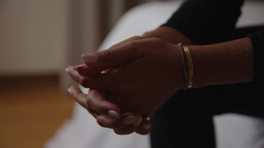 A lady seated on the bed with her two hands locked together