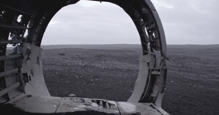 A wrecked airplane cabin sits in a rocky terrain on an overcast day