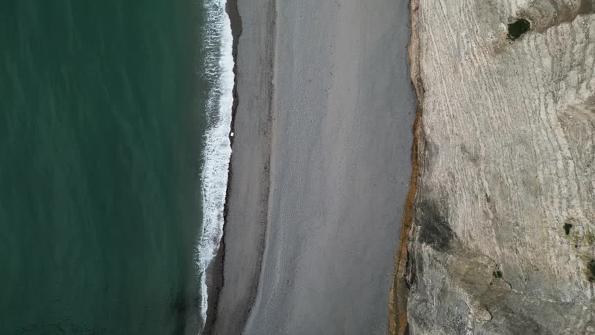 A beach that has a small strip of sand with one side facing the sea and the other a huge stone wall
