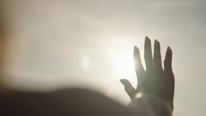 A silhouette of a hand with fingers spread illuminated by the sun