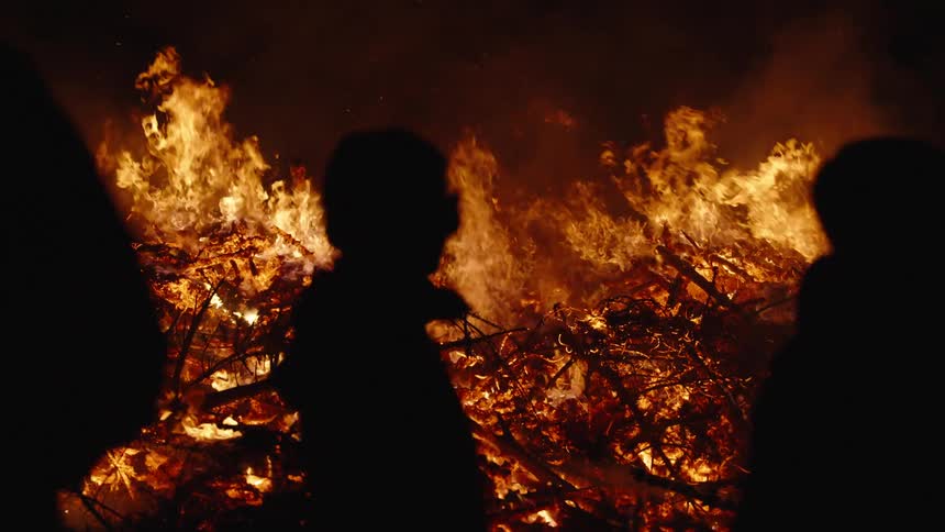 Silhouette of children next to a forest on fire at night