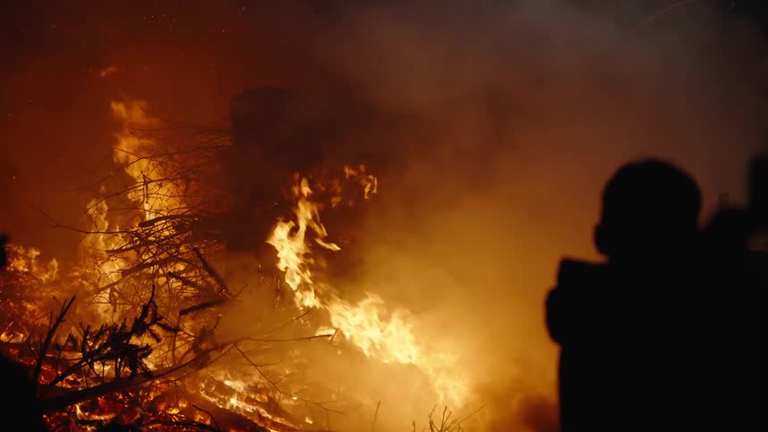 Silhouette of a family watching a large fire outdoors at night
