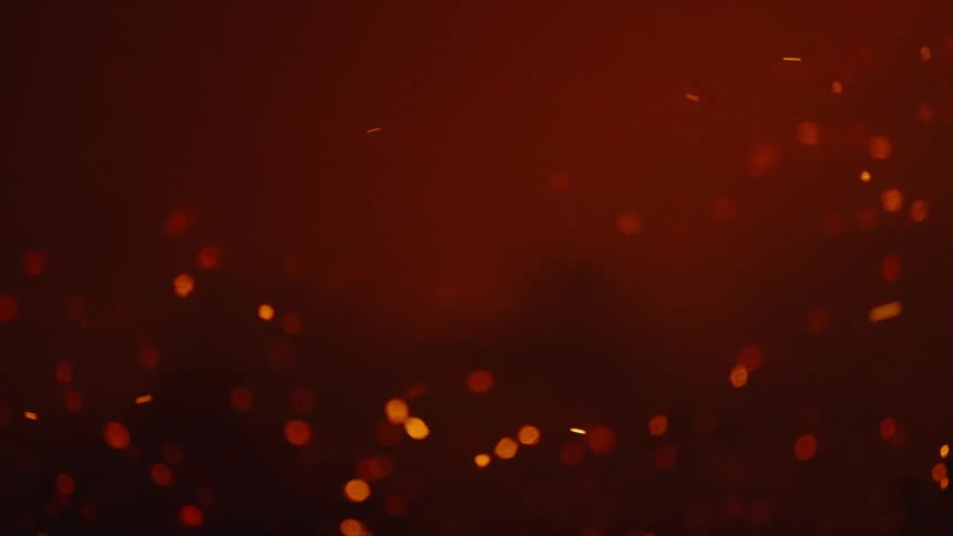Sparks from a fire fall on the ground and float in the nigth sky