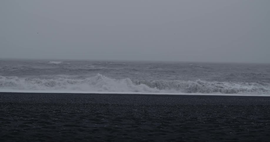 Waves crash on a beach with black sand