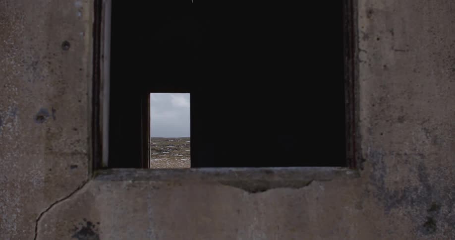 An empty, stained concrete building in a sandy area