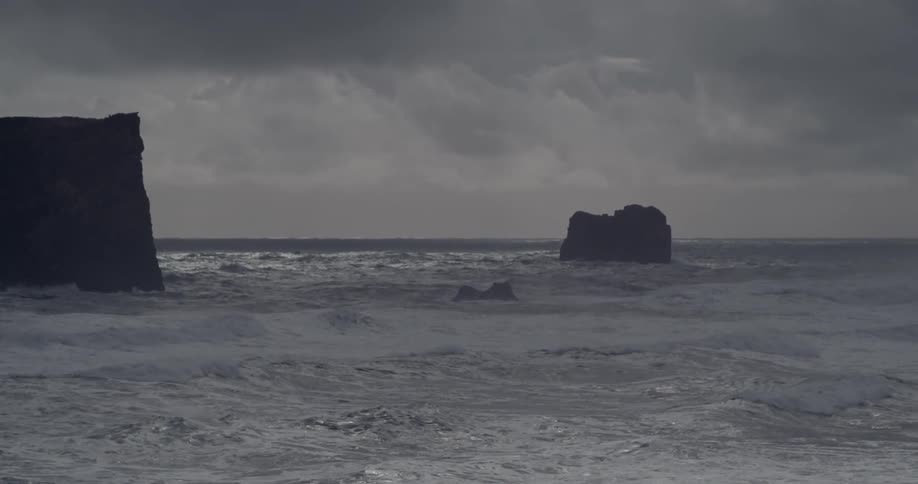 A choppy ocean with rocks jutting out of it on a cloudy day