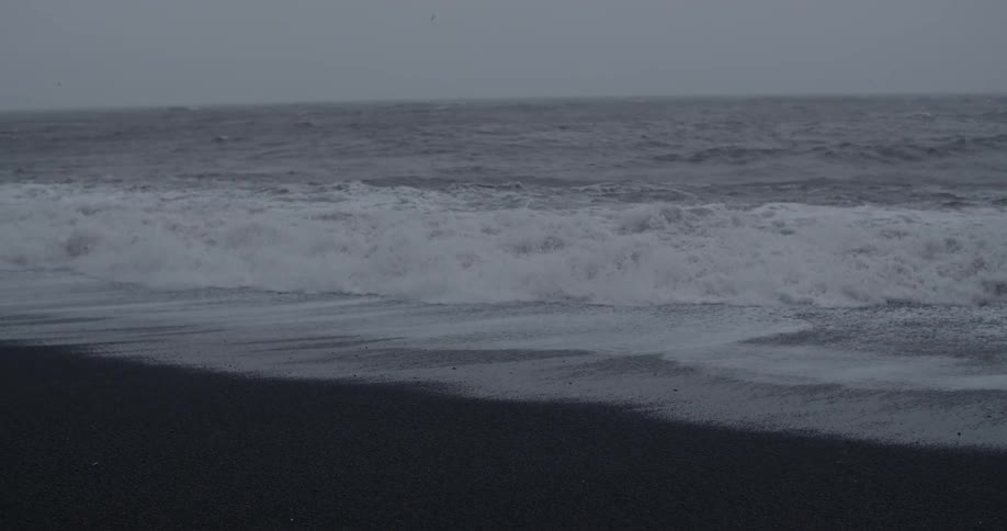 A large wave crashes ashore on an overcast day
