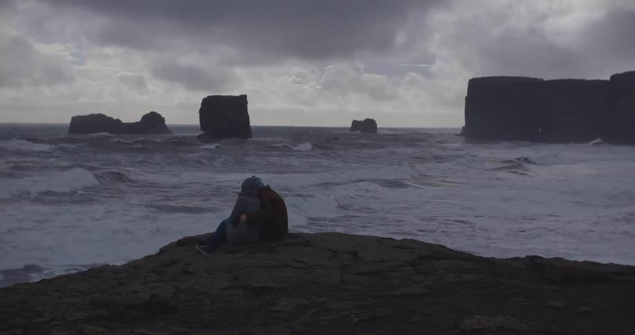 A couple sits on a rock watching the ocean waves