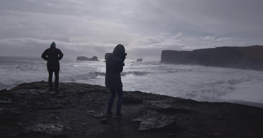 Two people standing on solid ground while waterside on a very cloudy day