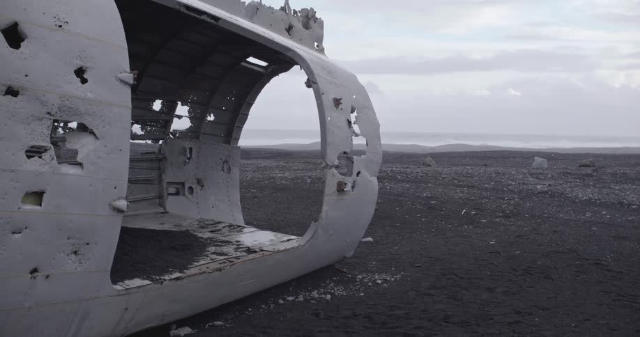A wrecked plane fuselage sits on black sand