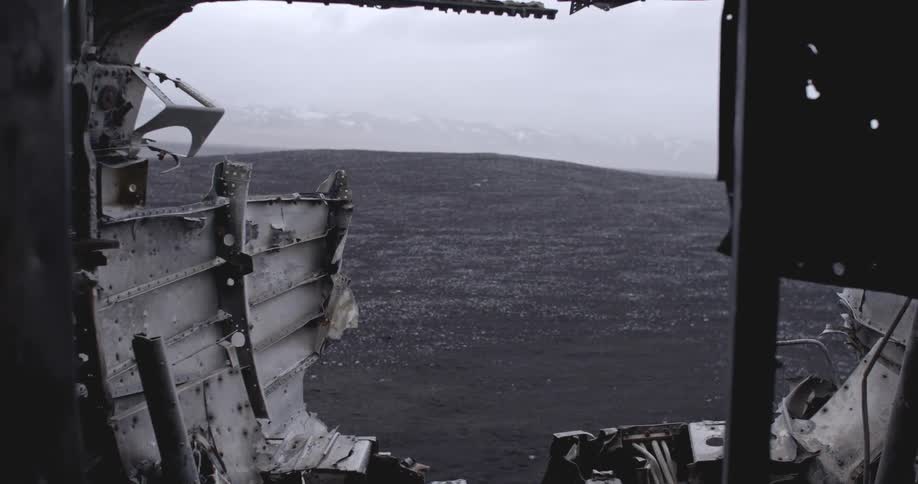A wrecked airplane cabin sits in a rocky terrain on an overcast day