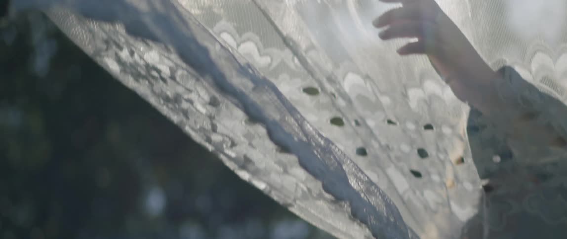 A person passing their hand over a veiled garment that is stiff and receiving sunlight