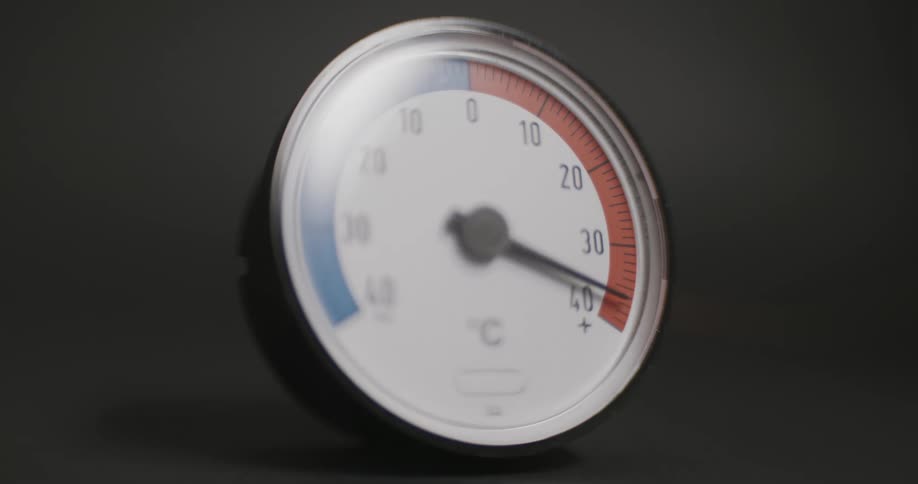 A closeup of a round thermometer slowly rising in temperature