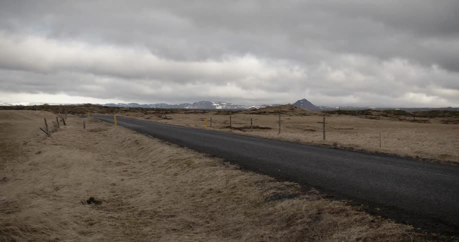 Mountains and clouds loom on the horizon beyond an empty rural road