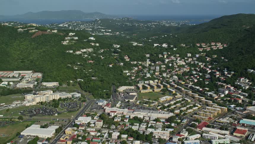 Aerial panorama of a residential neighborhood with houses and apartments amidst hills and mountains with the sea on the horizon