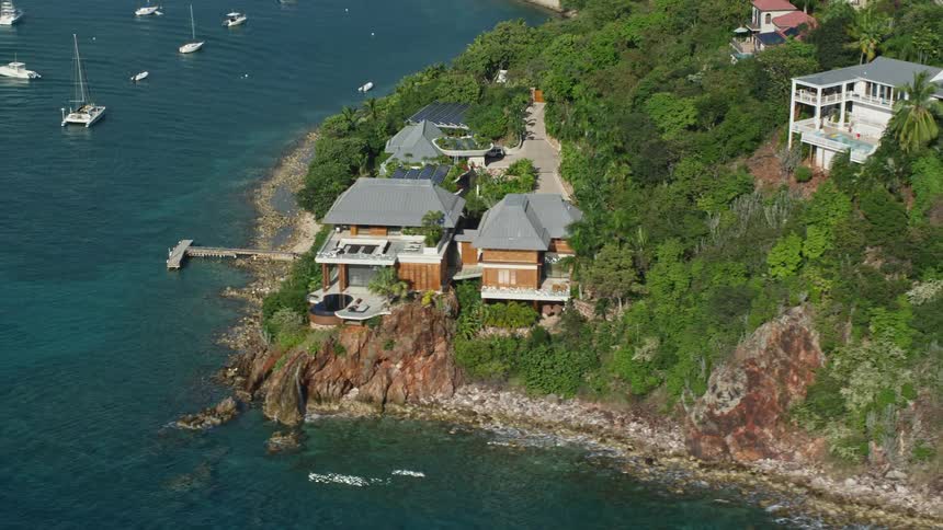 A residence on the coast of a sea with some boats parked and behind this house there are lots of trees and some other houses