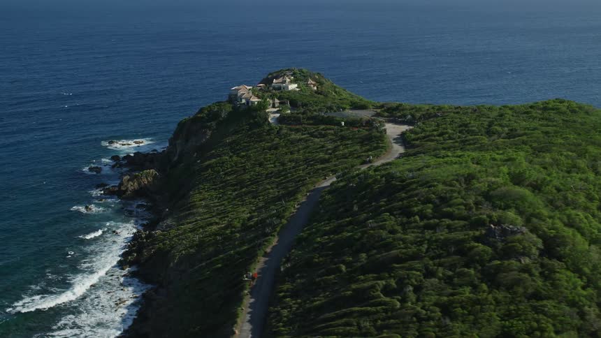 A small peninsula covered in vegetation except for a villa at the end and the road leading to it