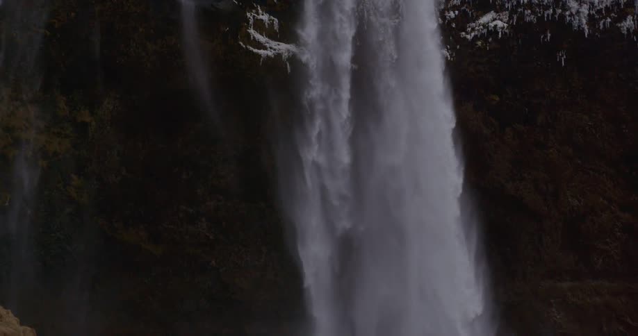 A waterfall flows over a snow cliff edge to a pool below