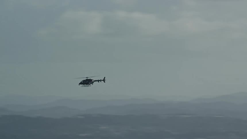 Helicopter flies over foggy urban landscape bordering mountains