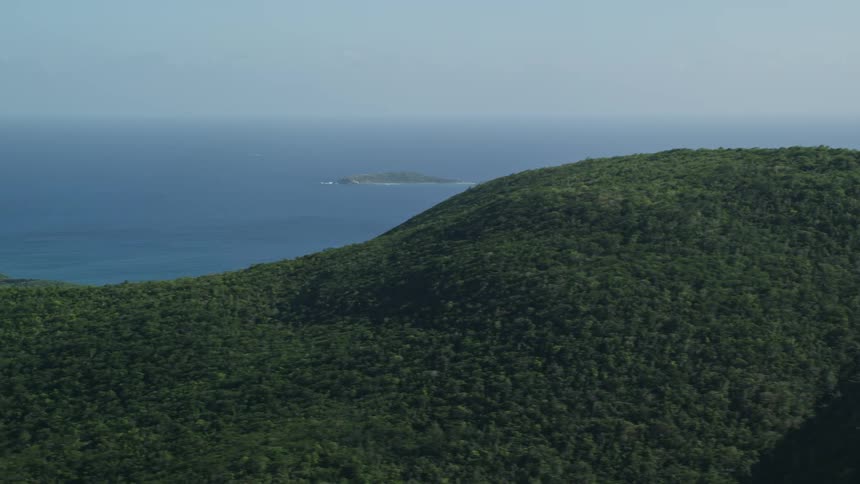 Aerial panorama of mountain ranges covered with vegetation facing the blue sea on a cloudless day