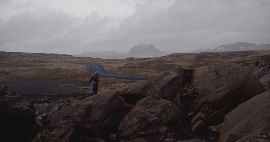 A man and woman walk in a rocky field on an overcast day while hugging