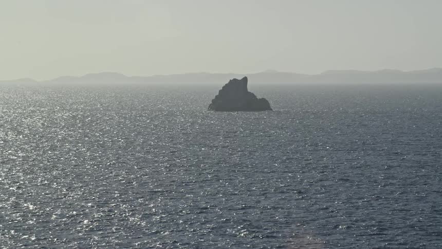 An aerial view of the ocean with a large rock jetting out of it