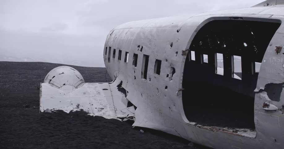 A wrecked airplane cabin sits in a rocky terrain on an overcast day