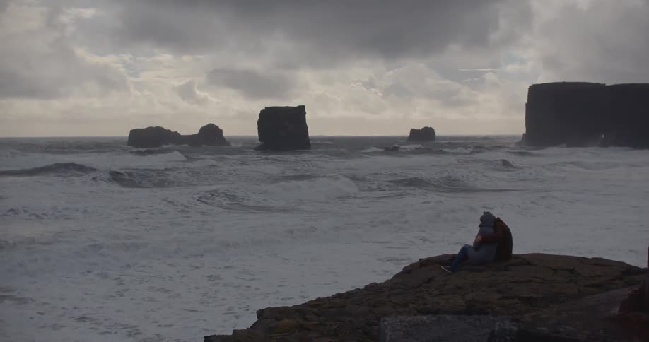 Waves crash ashore on the rocky shoreline as a couple embraces