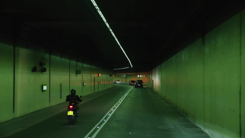 Motorcyclist follows cars on street passing through tunnel