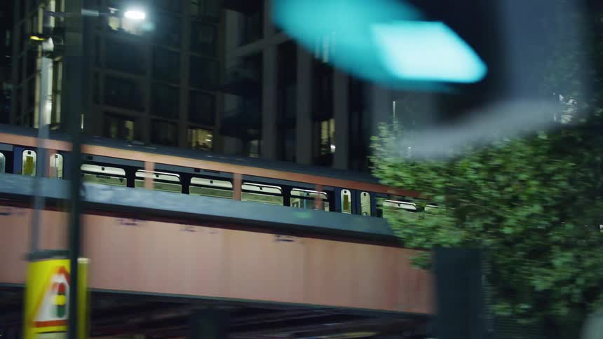 A train passes over a viaduct and there are several buildings behind it and trees and signs below