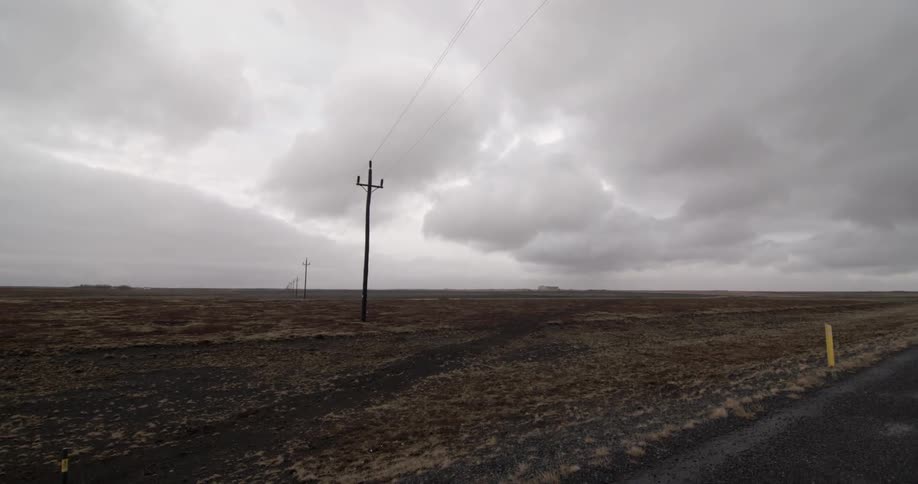 Telephone poles stretch out toward the horizon under a cloudy sky