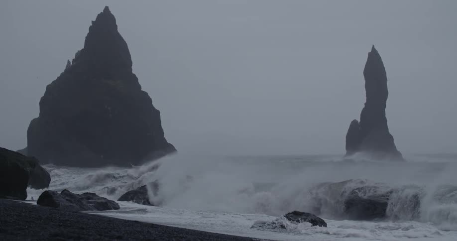 A large wave crashes ashore on an overcast day