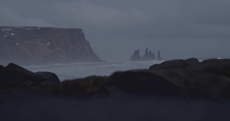 Waves crash near cliffs on a rocky shoreline on a stormy day