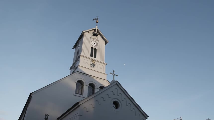 A white church's tower stands against a blue sky