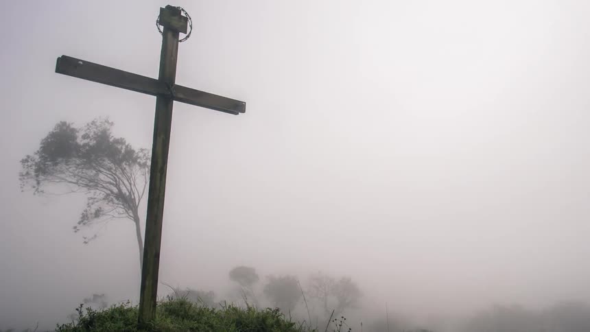 Fog rolls in on a mountaintop where a cross stands