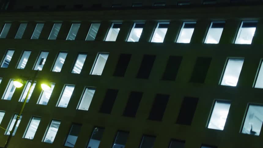 A red bus passing in front of a building with many windows at night