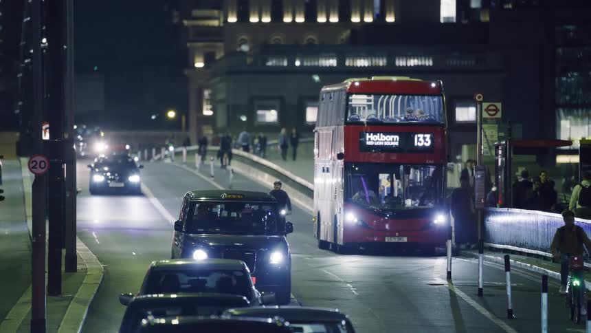Red double decker bus stops on street with cars and bikes at night