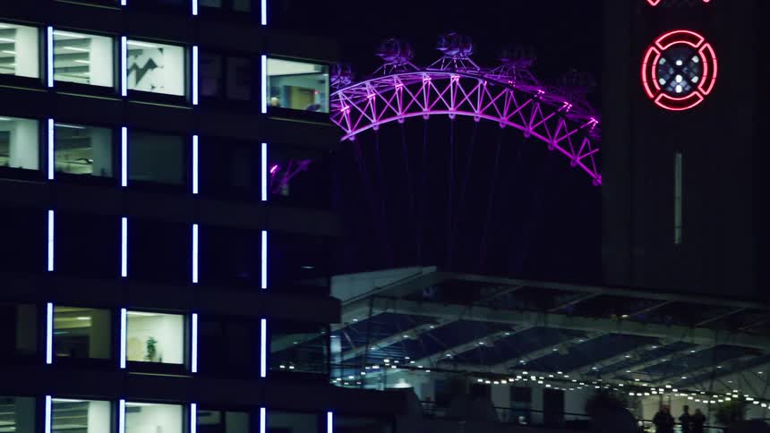 View of illuminated night buildings with a ferris wheel in the background with purple dot lights