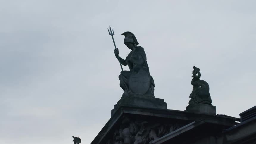 A statue on top of a building of a sitting guard holding a trident