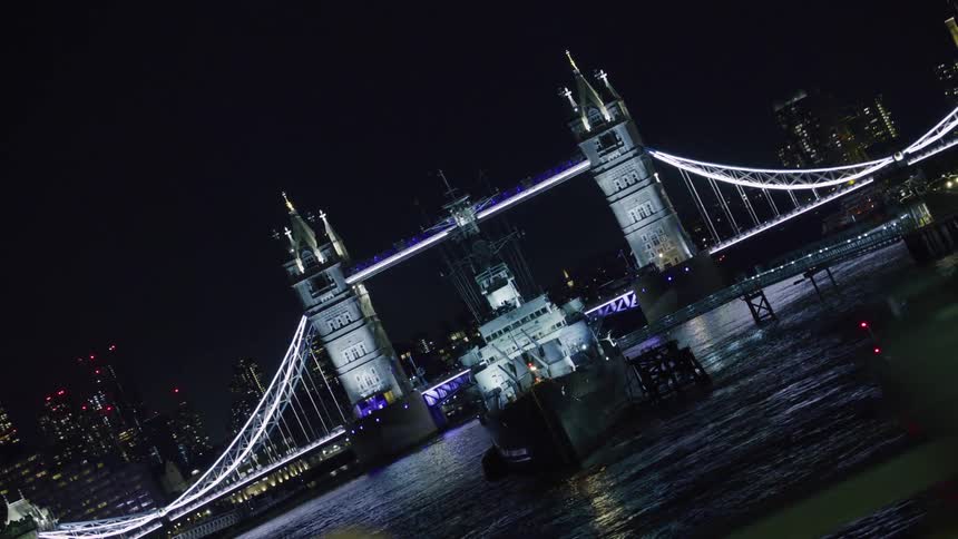 View of the london suspension bridge with a boat in front and buildings in the background on a night