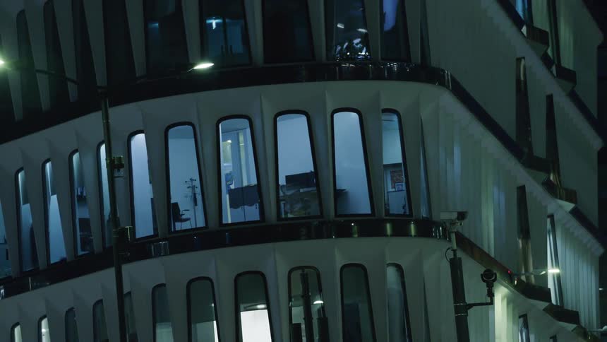 A modern building with curved architecture and large windows illuminated in the evening