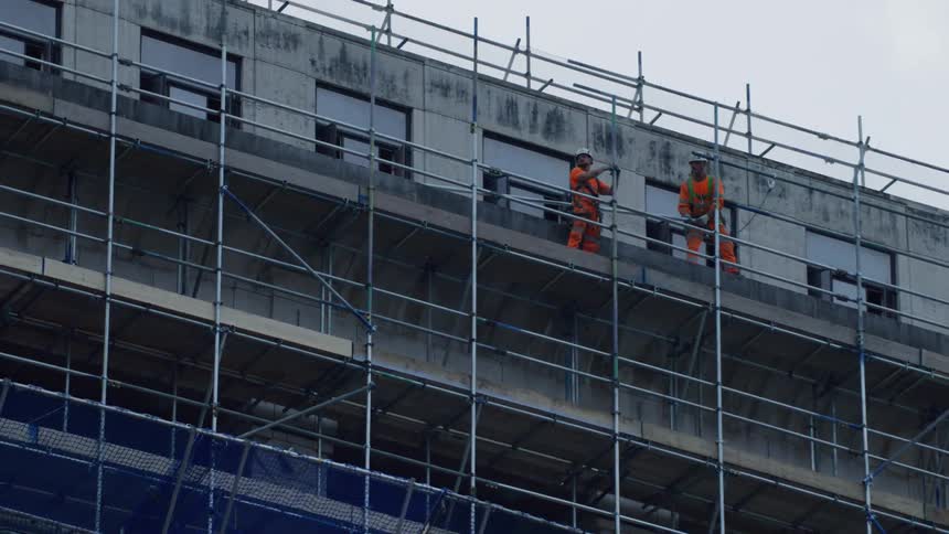 Two construction workers on top of a buildings scaffolding