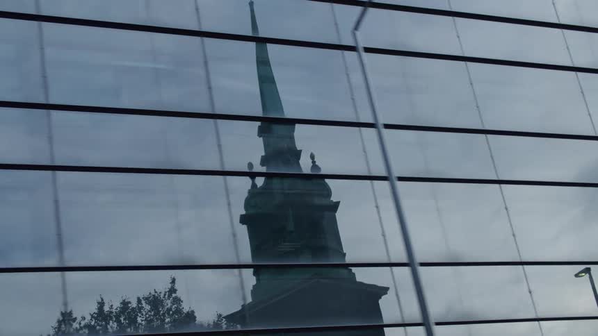 Building glass reflects nearby tower on a cloudy day
