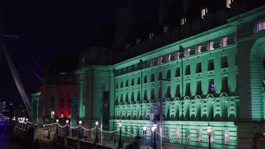 View of an illuminated building in london at night by a bridge and the sea