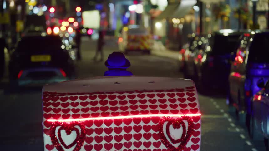 Man riding a bicycle with a trailer in the middle of a metropolis at night with cars around