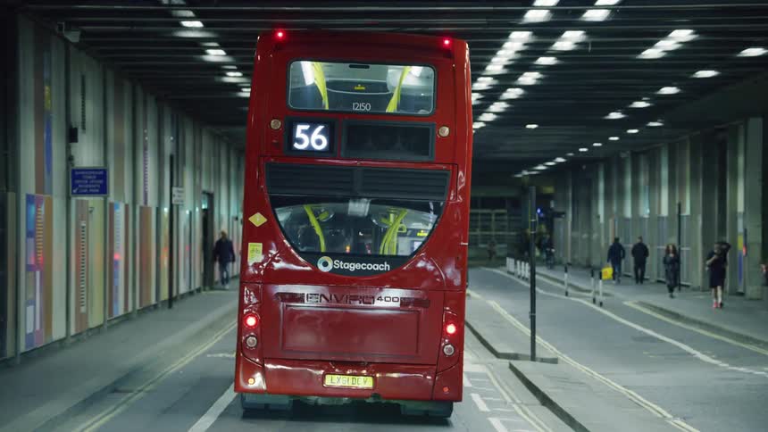 Red double decker bus under terminal lights at night